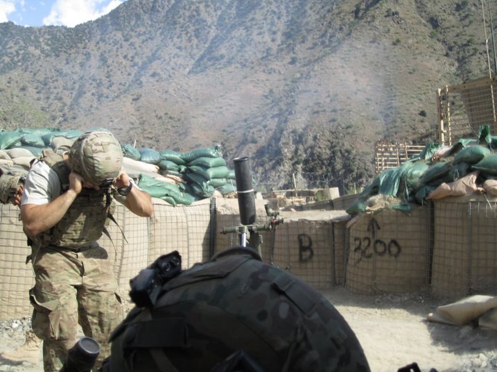 View of sandbags in front of mountains and soldier with hands in ears.
