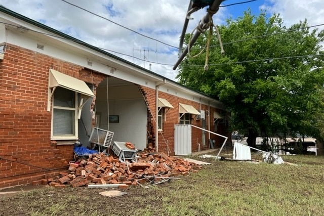 A house with one of its brick walls knocked outward. 