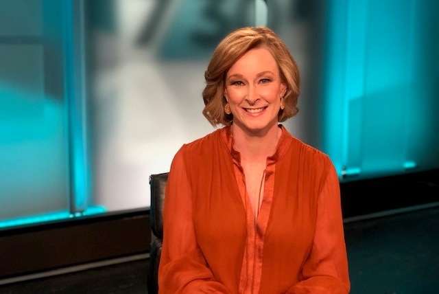 Journalist Leigh Sales sits in front of a 730 backdrop wearing an orange blouse.