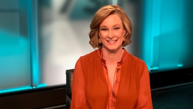 Journalist Leigh Sales sits in front of a 730 backdrop wearing an orange blouse.
