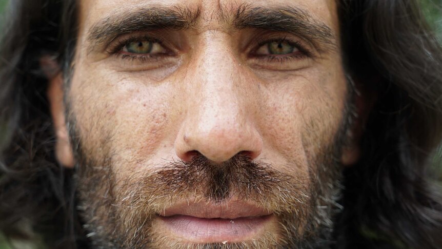 A close-up portrait of a man with a scruffy beard and piercing green eyes.