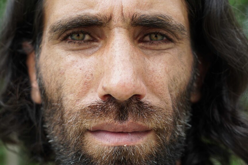A close up portrait of a man with a scruffy beard and piercing green eyes