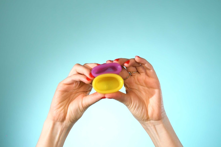 Two menstrual cups being squashed down by a woman's hands