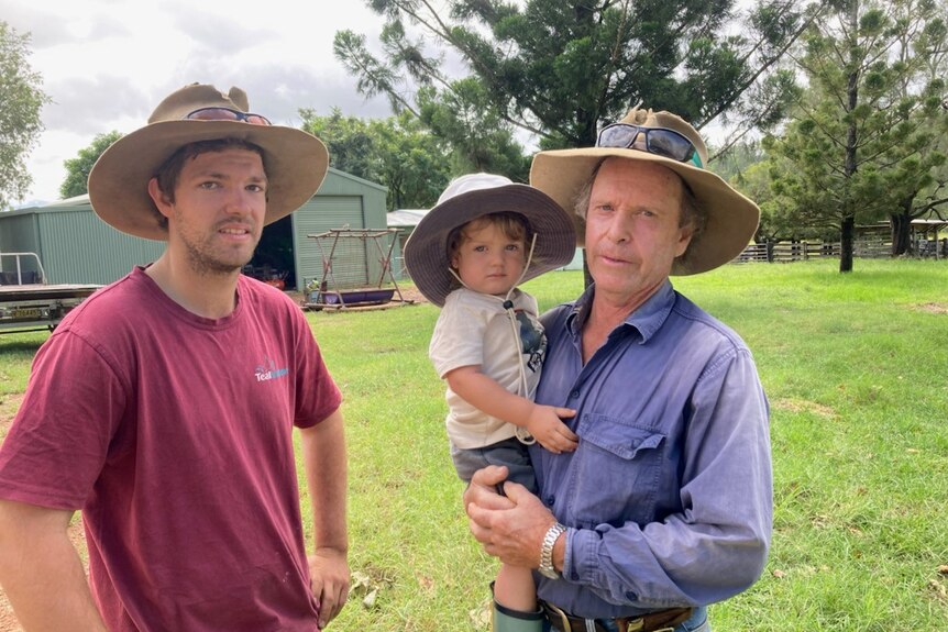 Two men standing in a yard wearing wide brim hats, one holding a small child in a wide brim hat