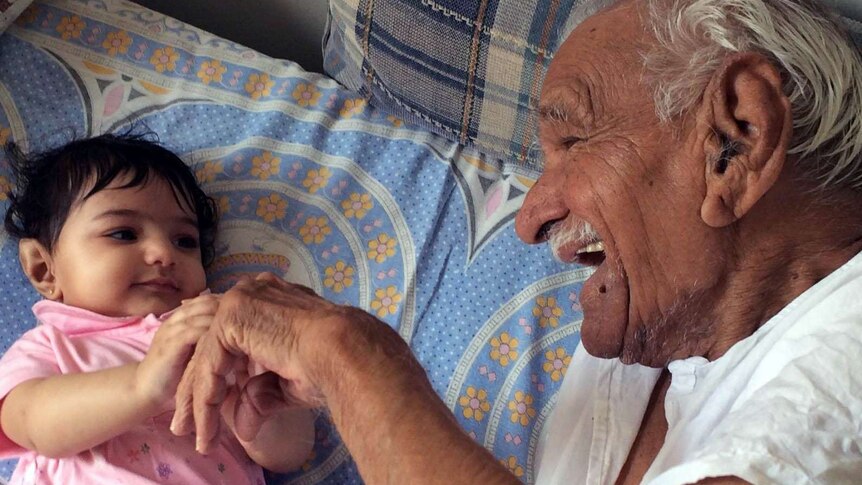 An elderly man and his granddaughter play together on a bed.