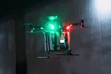 A drone hovers above the ground flashing a red and green light.