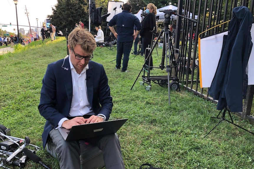 Lipson sitting on ground writing on laptop.