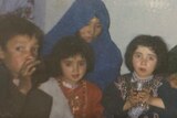A photo of a woman wearing a blue headscarf, with a boy to her left, and two girls in traditional clothing.