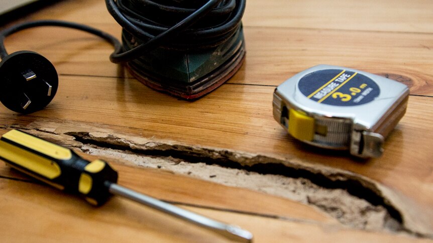 A sander, measuring tape and screwdriver sit next to a hole in floor boards.