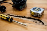 A sander, measuring tape and screwdriver sit next to a hole in floor boards.