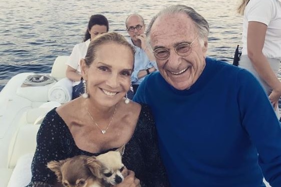 A smiling woman holding two dogs sitting never to a smiling man. They are aboard a yacht.