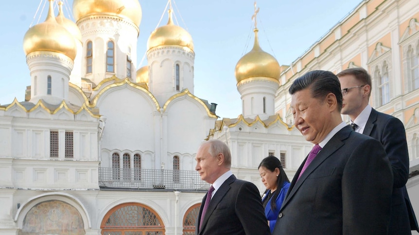 Vladimir Putin and Xi Jinping walk down stairs in front of a white and hold Orthodox church.