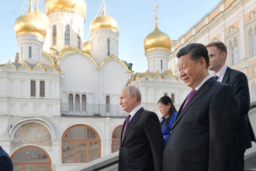 Vladimir Putin and Xi Jinping walk down stairs in front of a white and hold Orthodox church.