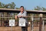 A photo of Lesley Munro leaning against a fence with 'authorised personnel only' signs on it. Some horse stables are visible.