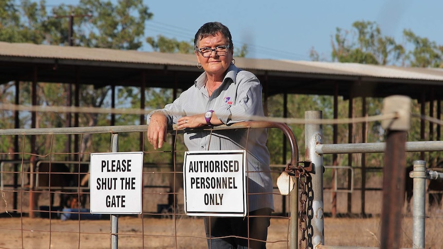 A photo of Lesley Munro leaning against a fence with 'authorised personnel only' signs on it. Some horse stables are visible.