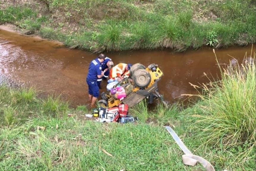 Emergency crews try to rescue a man from underneath a ride-on mower near a creek