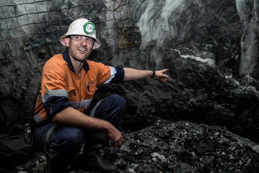 Mine worker underground points to visible gold on the wall.