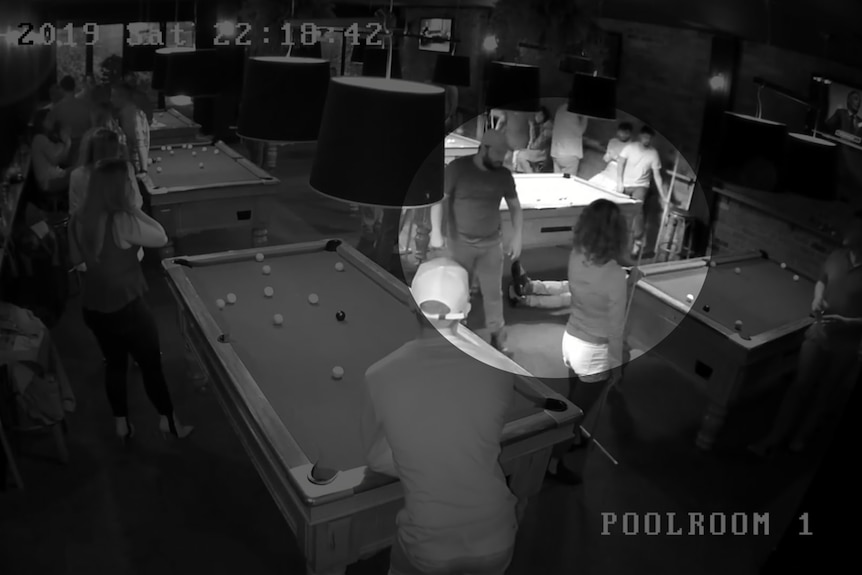 Black and white CCTV footage shows people standing around in a pool hall.