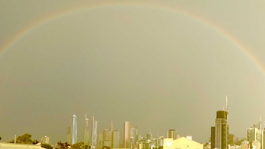 The Melbourne skyline turns a yellow colour, and a rainbow appears over buildings after a storm.
