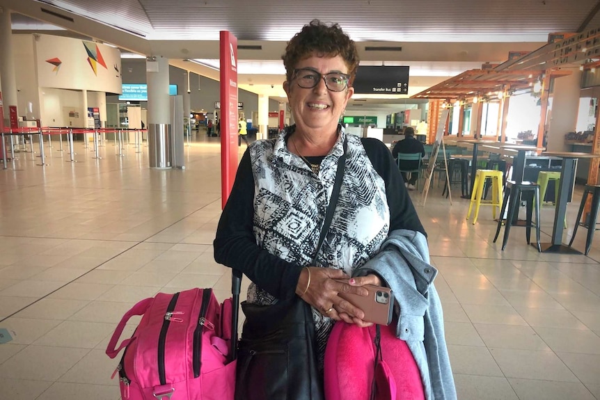 An older woman with pink luggage stands in an airport termimal