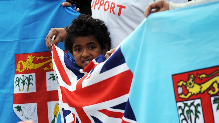 A Fijian child stands behind the flag