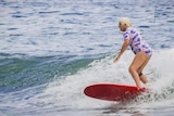 A woman in colourful togs catching a wave on a red surfboard