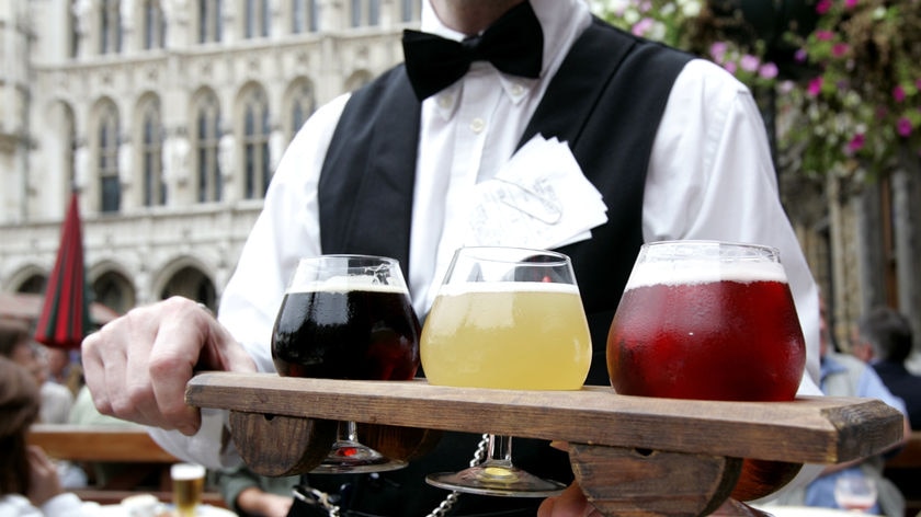 A waiter presents a plank of beers, in Belgian beer glasses