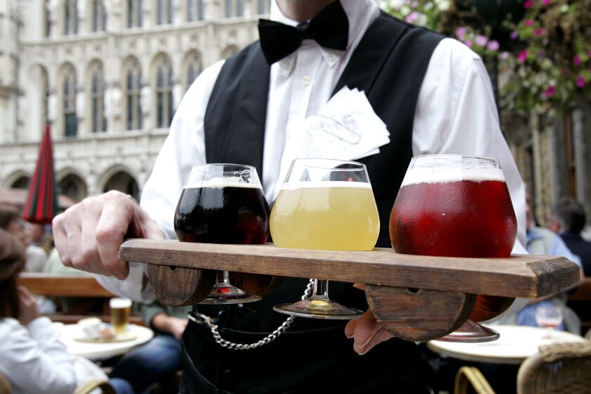 A waiter presents a plank of beers, in Belgian beer glasses