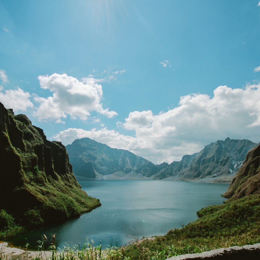 View of a large lake formed in a volcanic crater, with craggy, verdant mountains lining its shores. 