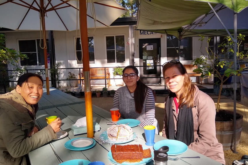 Three women at a picnic table sharing tea and cakes at a community garden in western Sydney.