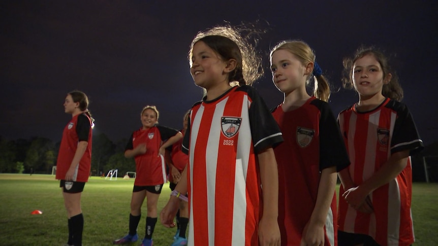 Girls with red and white striped soccer jerseys lining up at training.