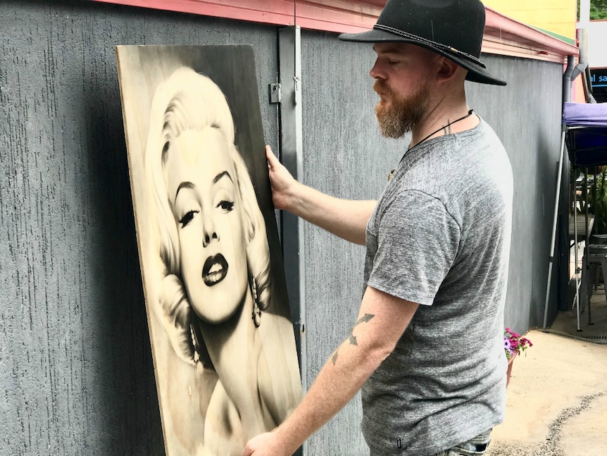 Man attempts to hang a large portrait of Marilyn Monroe on an outside wall of a building.