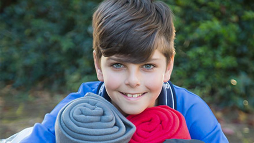 Young boy holding sleeping bags and blankets.