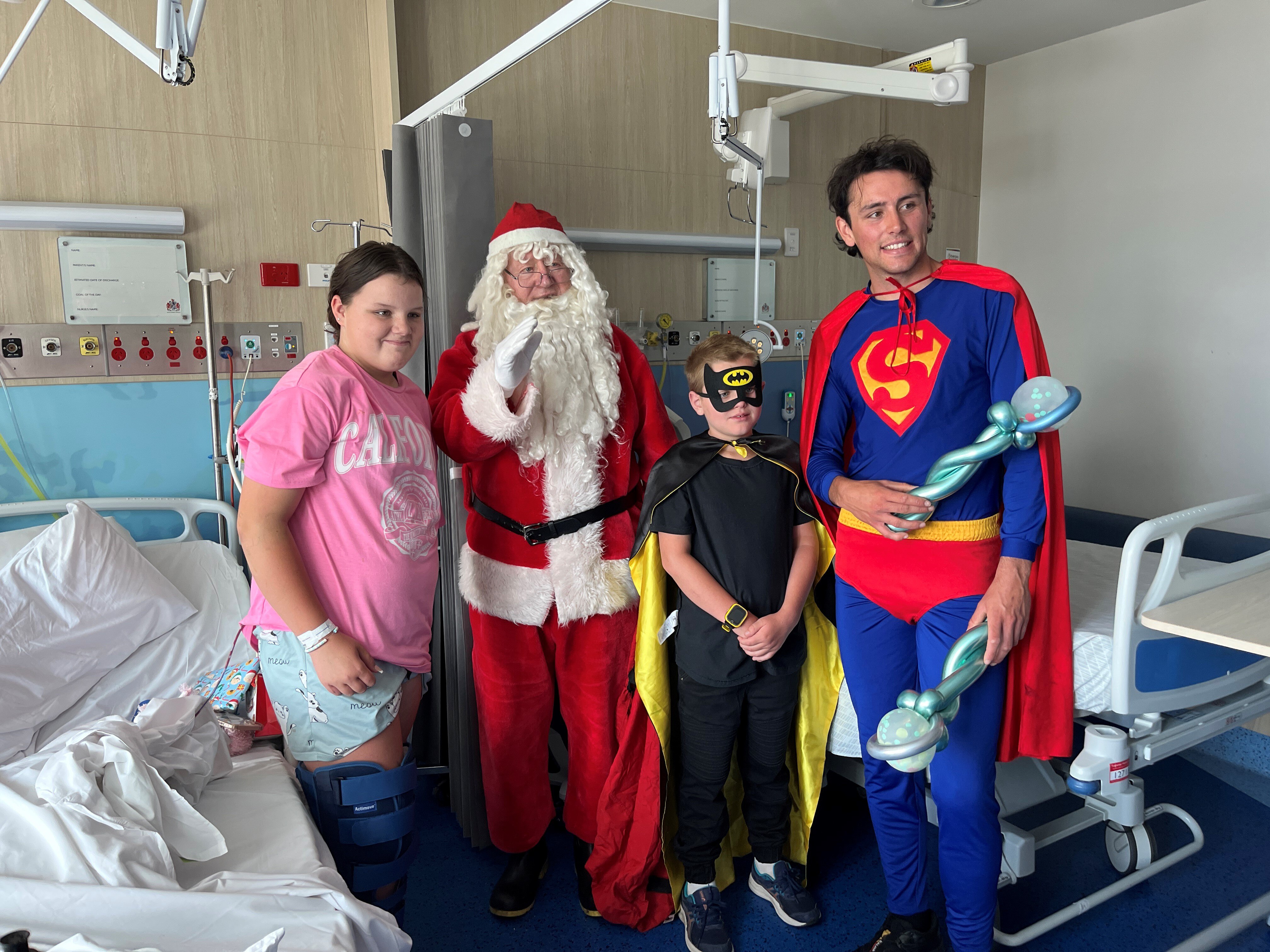 Three people dressed as Santa, Superman and Batman visit a child in hospital. 