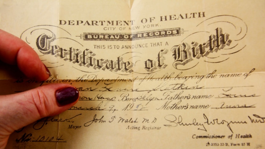 A woman's hand, with dark nail polish, holding a birth certificate