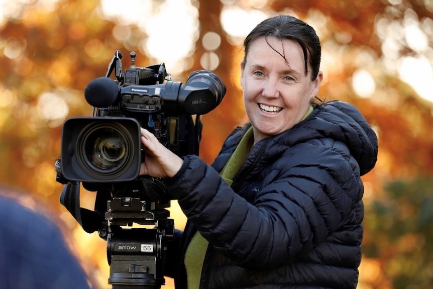 Woman operating camera with golden autumn leaves in the background.