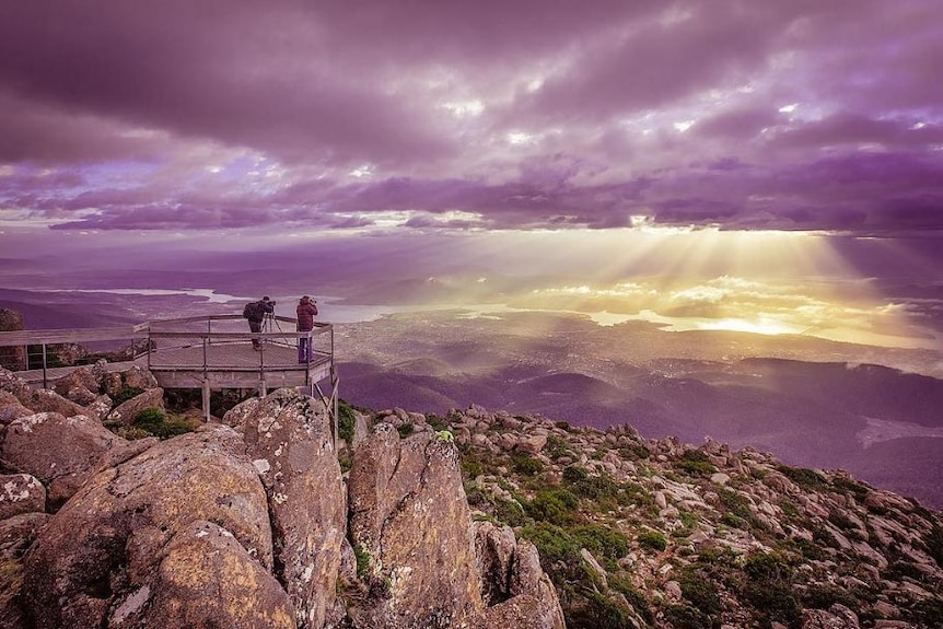 Wide view of two photographers standing on a lookout on top of Mt Wellington, photographing the sunrise.
