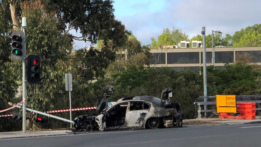 A burnt-out car sitting at the intersection of a road.