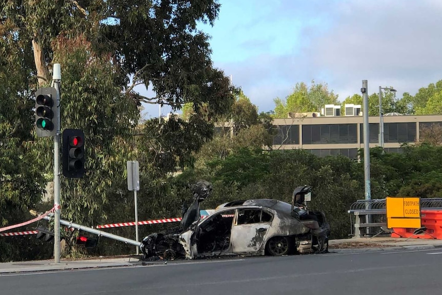 A burnt-out car sitting at the intersection of a road.