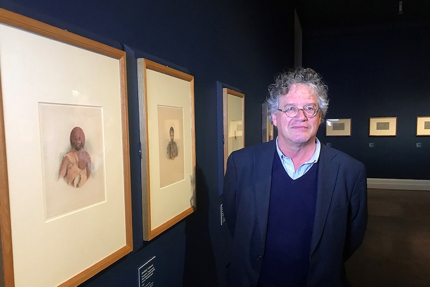 Jonathon Watkins stands in front of Thomas Bock paintings