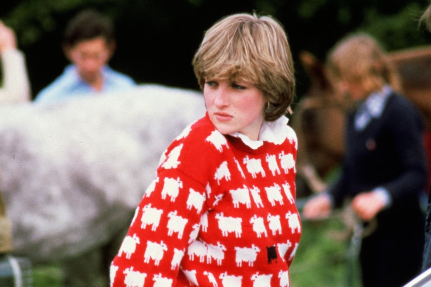 Princess Diana wearing a red jumper with white and black sheep. 