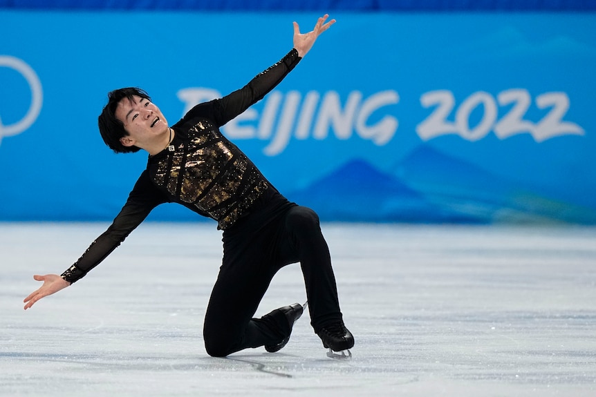 A young Japanese skater goes on one knee with arms spread in his finishing pose for his figure skating program.