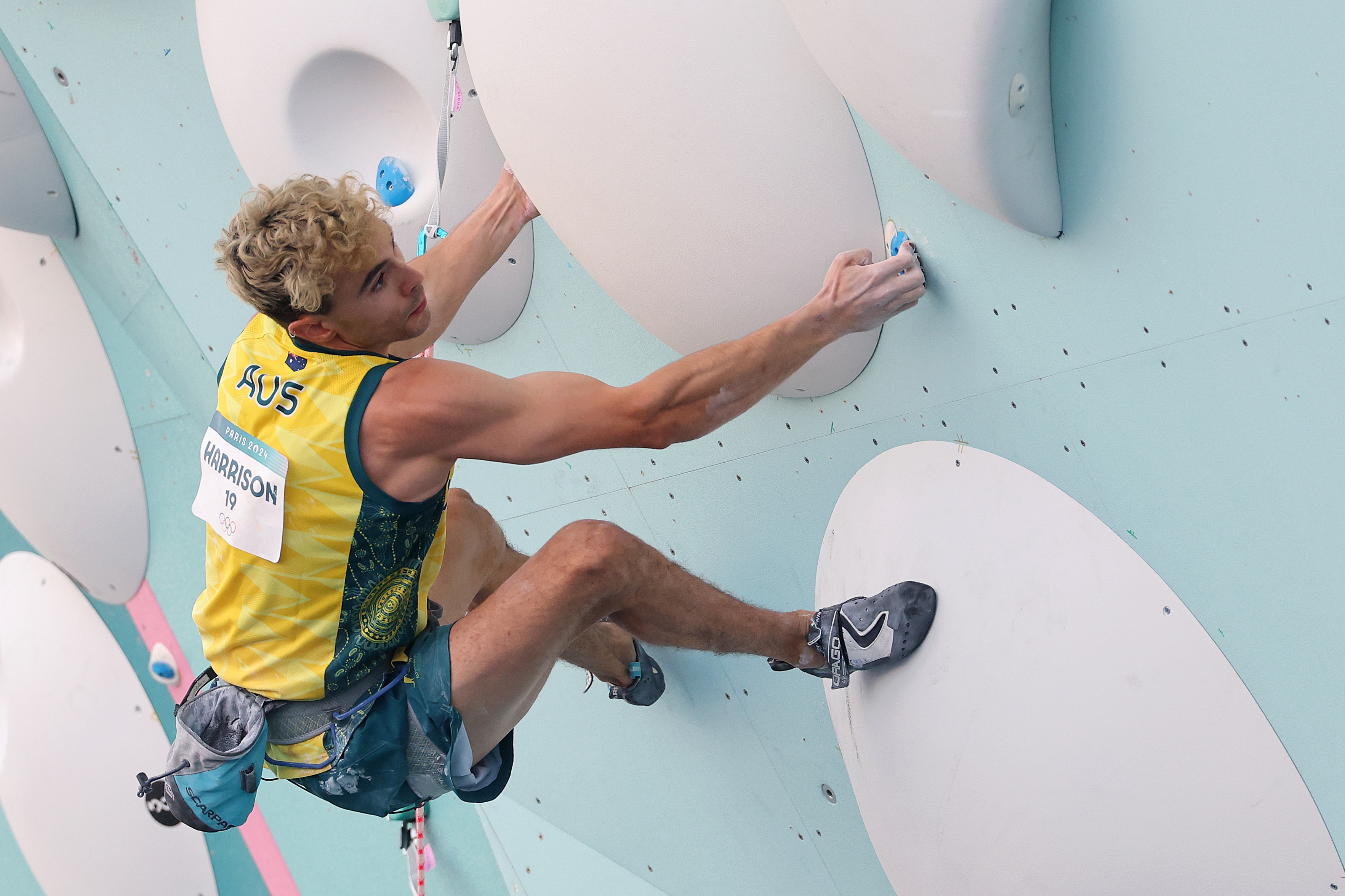 Un hombre de 27 años compite en una competición olímpica de escalada con el nombre de Harrison en la espalda.