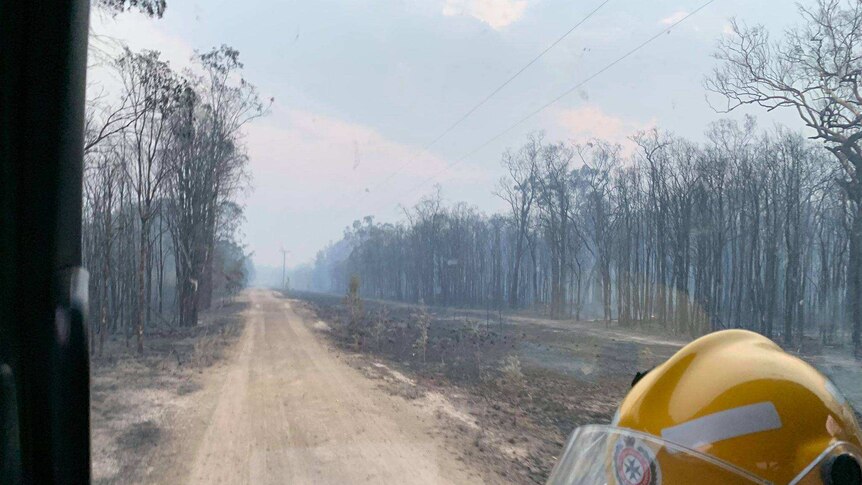 Shot of a truck window with a QFRS helmet and dirt road with charred trees in distance.