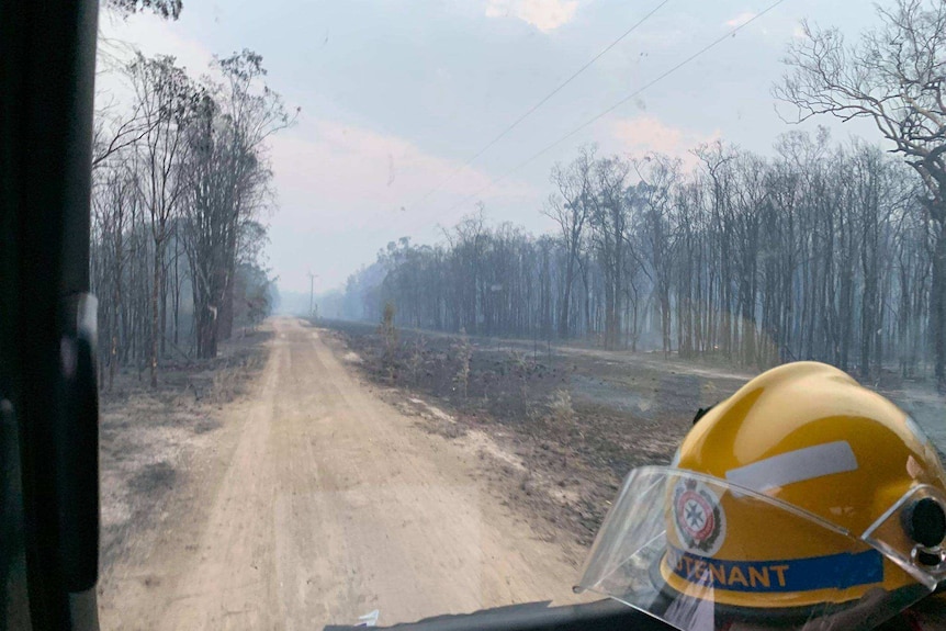 Shot of a truck window with a QFRS helmet and dirt road with charred trees in distance.