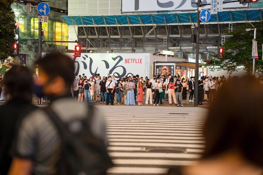 A crowd of people wait to cross Shibuya crossing in Tokyo 