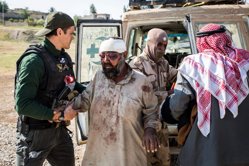 A man with heavily swollen eyes and a bandaged head is treated behind the armoured ambulance.