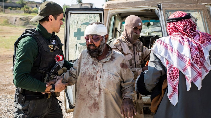 A man with heavily swollen eyes and a bandaged head is treated behind the armoured ambulance.