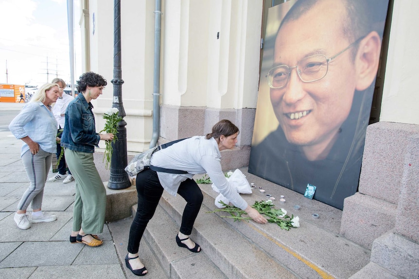 People place flowers and light candles in front a picture of Liu Xiaobo.