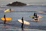 Surfers prepare to enter the water for a sunrise swim at a surf beach in New Zealand.
